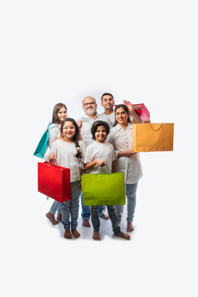 Multigenerational família indiana feliz segurando sacos de compras de papel e débito ou cartão de crédito, enquanto de pé isolado sobre fundo branco - Foto, Imagem