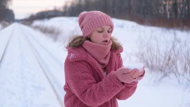 mulher jovem no casaco de peles falso rosa sopra neve de palmas no inverno. Movimento lento. retrato de uma mulher no inverno - Filmagem, Vídeo