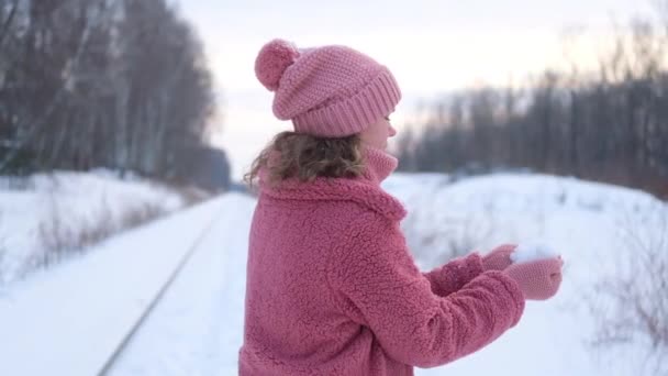 mujer joven en rosa abrigo de piel sintética sopla nieve de las palmas de las manos en invierno. En cámara lenta. retrato de una mujer en invierno - Metraje, vídeo