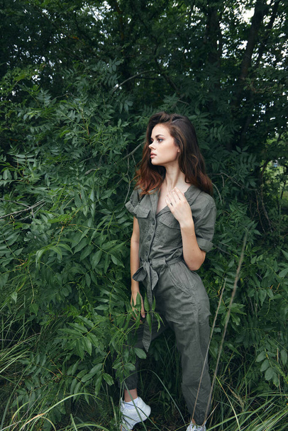 woman in forest in green overalls near the Bushes touches himself with a hand nature  - Foto, immagini
