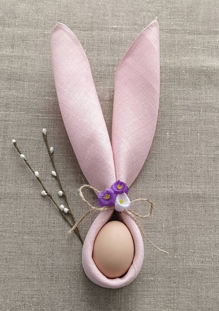 Dekorativní králík Uši z ubrousku s vejcem na přírodním bavlněném ubrusu na oslavu Velikonoc - Fotografie, Obrázek