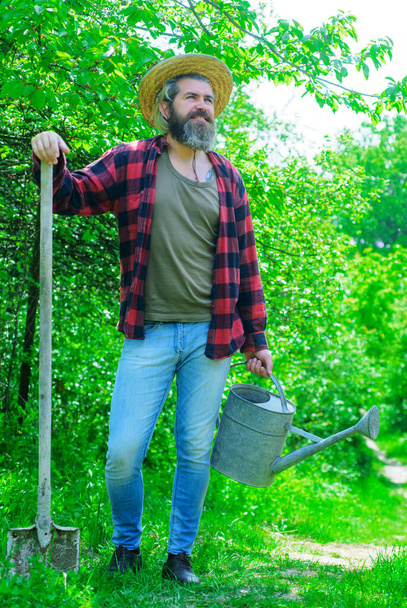Φάρμα. Χαμογελώντας άνθρωπος με ποτιστήρι και φτυάρι. Ο αγρότης ετοιμάζεται να φυτέψει. Κηπουρική. Σπαθί κήπου. - Φωτογραφία, εικόνα