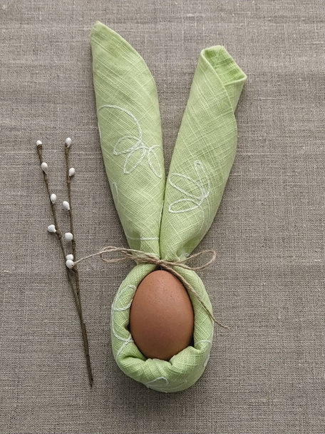 Уши кролика из зеленой салфетки с яйцом на скатерти из натурального хлопка, чтобы праздновать Пасху - Фото, изображение