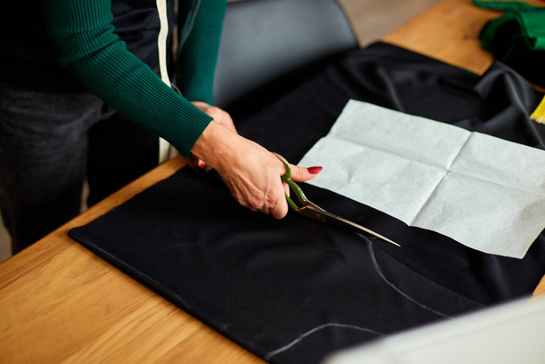 段階的に、女性のドレスメーカーの手は、テーブルの上にはさみで材料を切断し、アトリエ、繊維産業、趣味、ワークスペースで働く成熟した仕立て屋。作成プロセス｜DIY 、シームレスストレスの職場. - 写真・画像