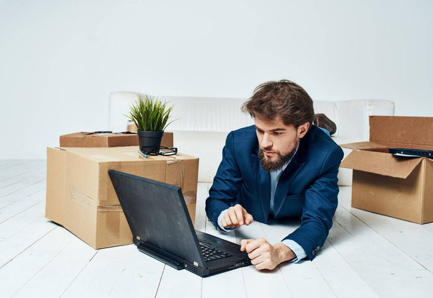 Un hombre de negocios yace en el suelo frente a una computadora portátil, trabaja sin cosas desempaquetadas - Foto, Imagen