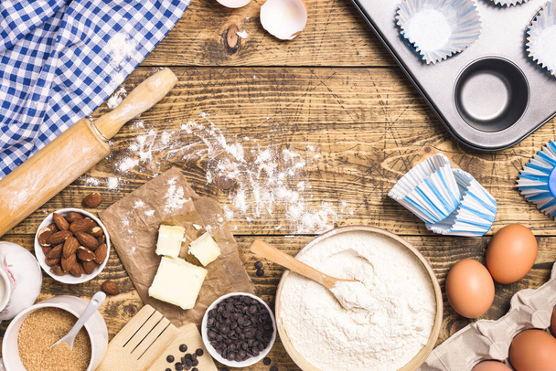 材料や道具で焼き菓子やケーキを調理するフレーム。小麦粉、砂糖、牛乳、卵、バター、アーモンドテキスト、フラットレイアウトのためのコピースペースを持つ素朴な木製の背景に. - 写真・画像
