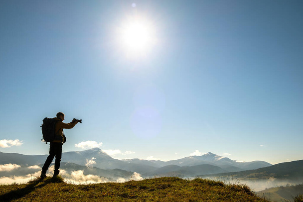 Silueta de un fotógrafo de mochilero tomando fotos del paisaje matutino en las montañas de otoño con cámara digital. - Foto, Imagen