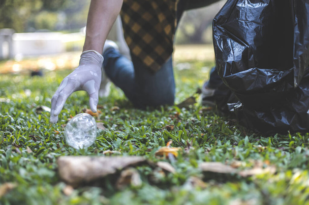 Mężczyźni wolontariusze nosić butelki wody lub plastikowe torby, które spadły w parku umieścić je w koszu na śmieci, Ochrona środowiska lub wolontariatu na cele charytatywne, Usuwanie odpadów poprzez recykling. - Zdjęcie, obraz