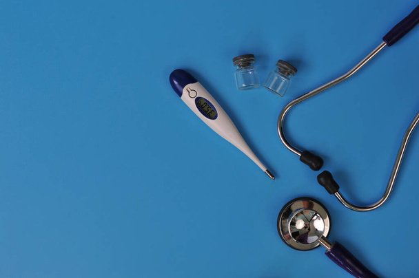 Układ stetoskopu, termometru i szklanych fiolek z pustym miejscem na tekst na niebieskim tle - Zdjęcie, obraz