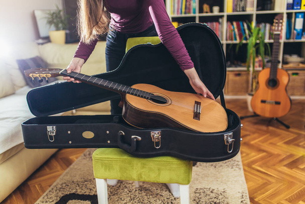 Жінка спостерігає і кладе класичну коричневу гітару з чорного футляру
 - Фото, зображення