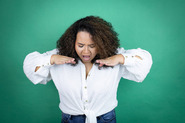 Młoda Afroamerykanka w białej koszuli na zielonym tle krzyczy i krzyczy głośno z rękami na ustach - Zdjęcie, obraz