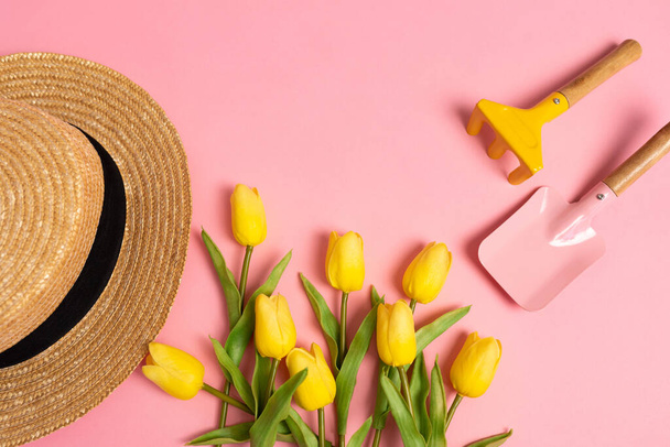 Attrezzatura da giardino con tulipani gialli e cappello di paglia su sfondo rosa. Vista dall'alto. Ricevuto. Giardinaggio Primavera Estate Concetto - Foto, immagini