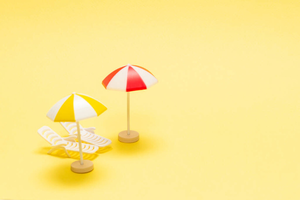 Két napozó és egy piros esernyő sárga háttérrel. Fénymásolási hely. - Fotó, kép