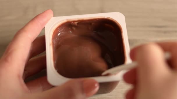 Zbliżenie rąk człowieka wziąć pyszne mus czekoladowy lub pudding z łyżeczką w plastikowym słoiku - Materiał filmowy, wideo