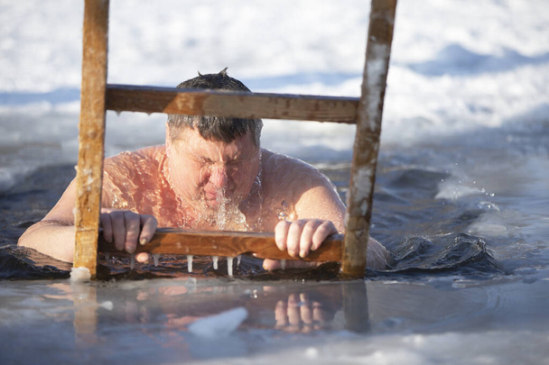 Ένας άνθρωπος βυθίζεται σε μια τρύπα πάγου κατά τη διάρκεια της χειμερινής γιορτής του βαπτίσματος του Ιησού. Ένας άντρας κολυμπάει στην τρύπα του πάγου το χειμώνα. Θαλάσσιοι ίπποι. - Φωτογραφία, εικόνα