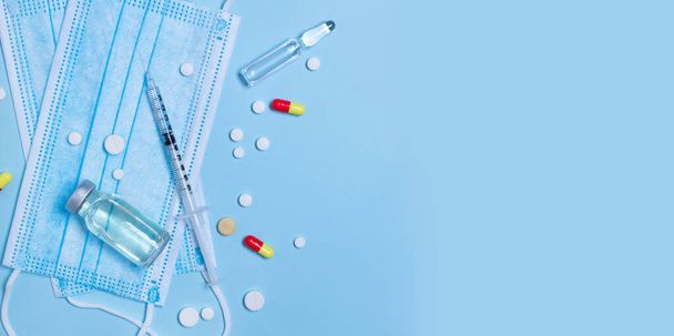 Top view orvosi összetétele fecskendő gyógyszeres, antibiotikum injekciós üveg, tabletták, tabletták és védő maszk kék alapon copypys. - Fotó, kép
