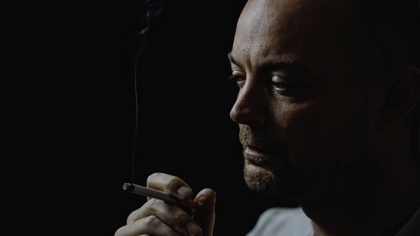 Sigara içen genç bir adamın düşünceli ve stresli halini yakından çek. Siyah arka planda izole edilmiş. Yüzeyin derinliği. Yüksek kalite fotoğraf - Fotoğraf, Görsel