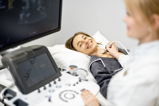 Врач, осматривающий щитовидную железу пациентки с помощью УЗИ в клинике - Фото, изображение