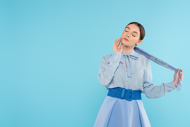 donna glamour toccare fazzoletto mentre in piedi con gli occhi chiusi isolati su blu - Foto, immagini