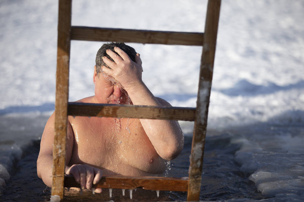 Un hombre se sumerge en un agujero de hielo durante la fiesta de invierno del bautismo de Jesús. Un hombre nada en el agujero de hielo en invierno. Gente morsa. - Foto, imagen