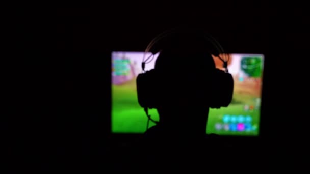 Silhouette eines jungen Spielers, der ein Headset trägt, während er ein beliebtes Shooter-Spiel spielt. Geringe Tiefenschärfe. - Filmmaterial, Video