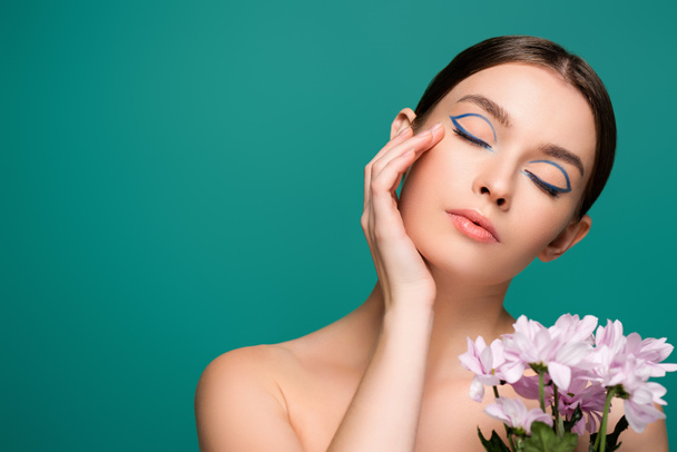 young woman with blue eyeliner on closed eyes posing near pink chrysanthemums isolated on green - Foto, Imagen