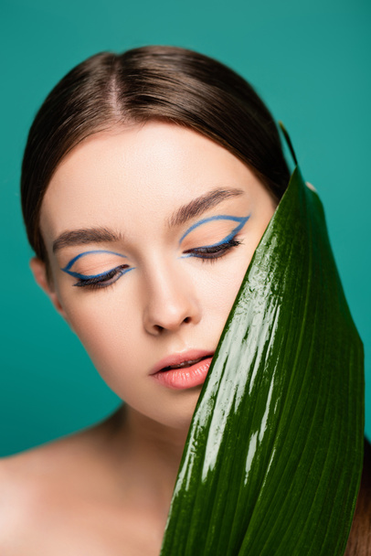 Porträt einer jungen Frau mit blauem Eyeliner, fast glänzendem Blatt isoliert auf Grün - Foto, Bild