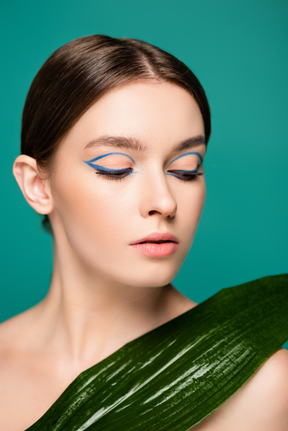 jeune femme sensuelle avec eye-liner bleu près de la feuille humide isolé sur vert - Photo, image