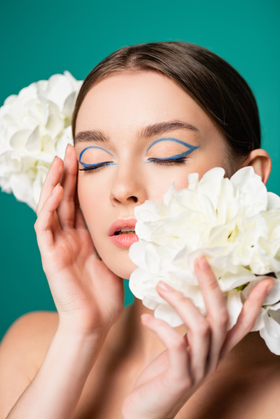 charming woman with blue eyeliner on closed eyes posing with white peonies isolated on green - Φωτογραφία, εικόνα