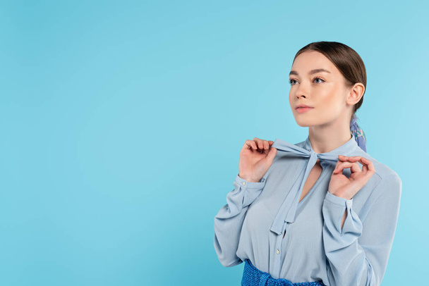mulher na moda olhando embora enquanto tocando arco na blusa isolado no azul - Foto, Imagem