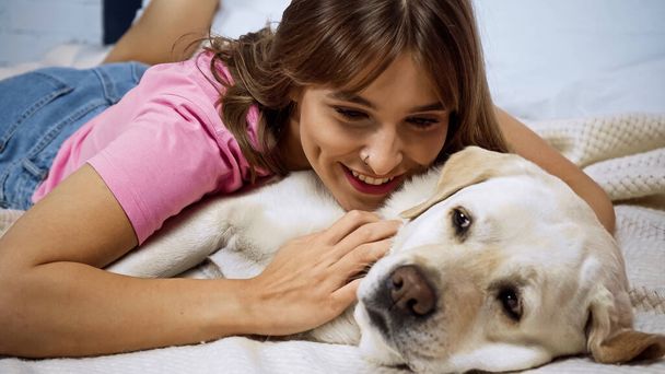 счастливая молодая женщина, лежащая с золотой собакой-ретривером на кровати - Фото, изображение