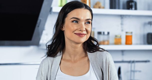 Brunette woman looking away and smiling in kitchen  - Photo, Image