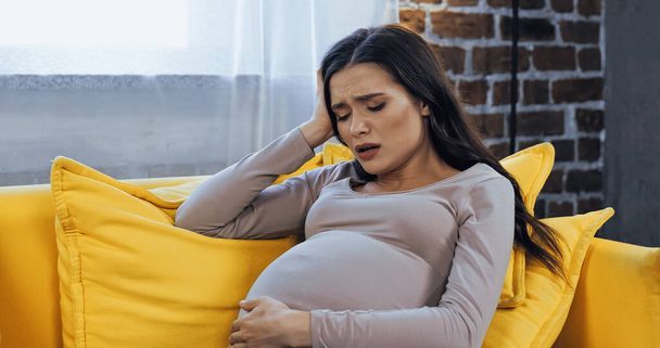 Upset pregnant woman sitting on couch  - Valokuva, kuva