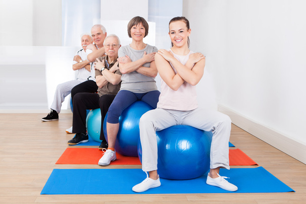 Entrenador y clientes mayores sentados en bolas de fitness
 - Foto, imagen