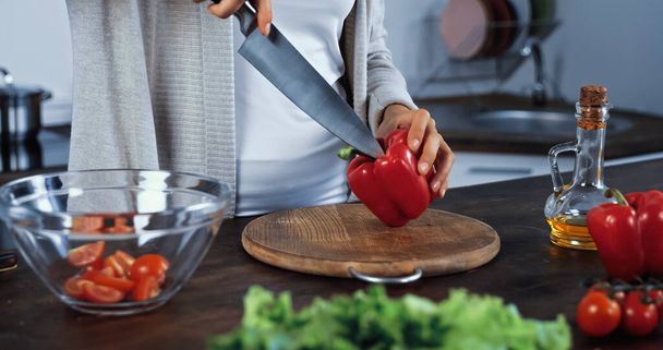Cropped view of woman holding knife and bell pepper near vegetables on blurred foreground  - Foto, afbeelding