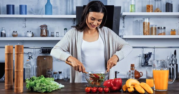 Smiling woman mixing salad near fresh ingredients  - Foto, immagini