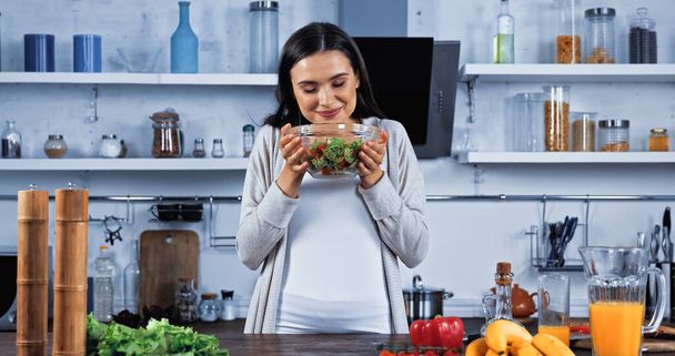 Usmívající se žena drží misku s čerstvým salátem v blízkosti zeleniny a pomerančového džusu  - Fotografie, Obrázek
