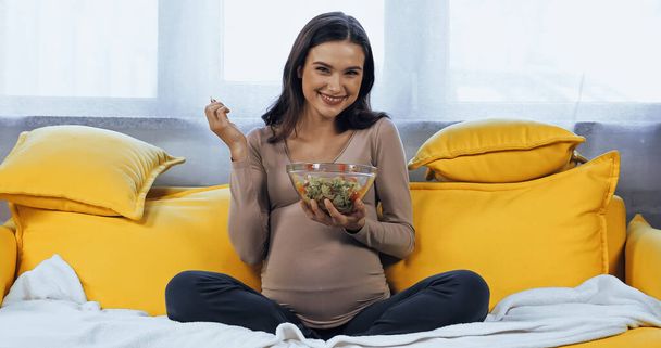 Smiling pregnant woman holding bowl with fresh salad  - Фото, изображение