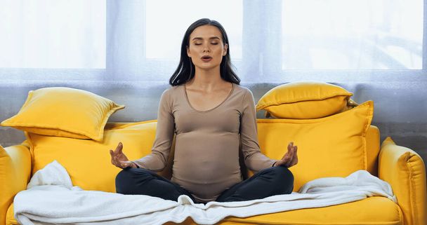 Těhotná žena medituje na gauči doma  - Fotografie, Obrázek