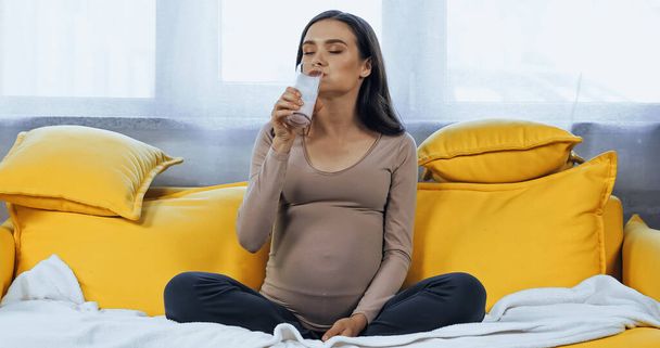 Pregnant woman drinking milk in living room  - 写真・画像