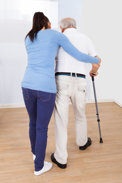 Caregiver Assisting Senior Man To Walk With Stick - Foto, imagen