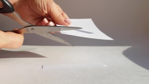 La mano di una donna taglia un foglio di carta bianca con le forbici e taglia gli angoli. Primo piano, concetto fai da te - Filmati, video
