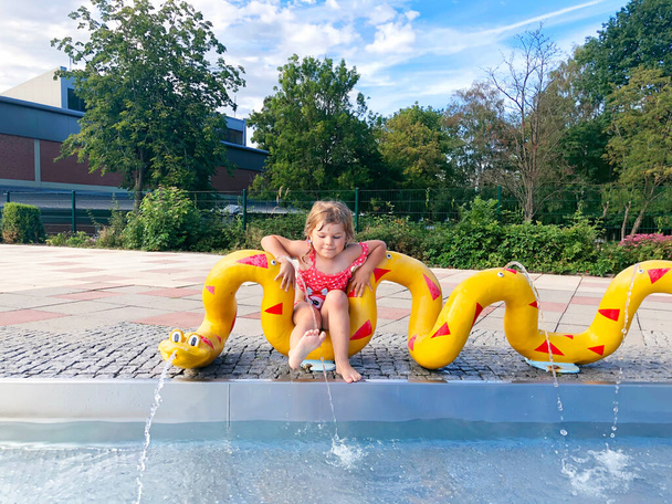 Pequeña niña chapoteando en una piscina al aire libre en el cálido día de verano. Feliz niño sano disfrutando de un clima soleado en la piscina pública de la ciudad. - Foto, imagen