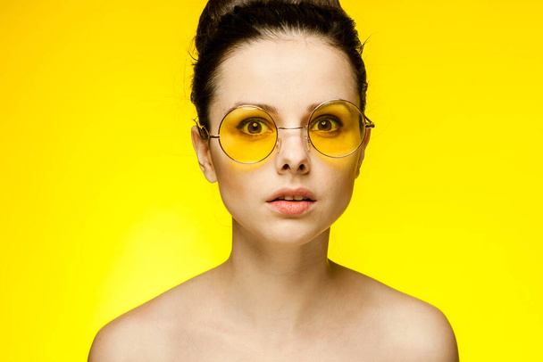 brunetka z gołymi ramionami noszenie żółte okulary przycięte widok pojedyncze tło emocje moda - Zdjęcie, obraz