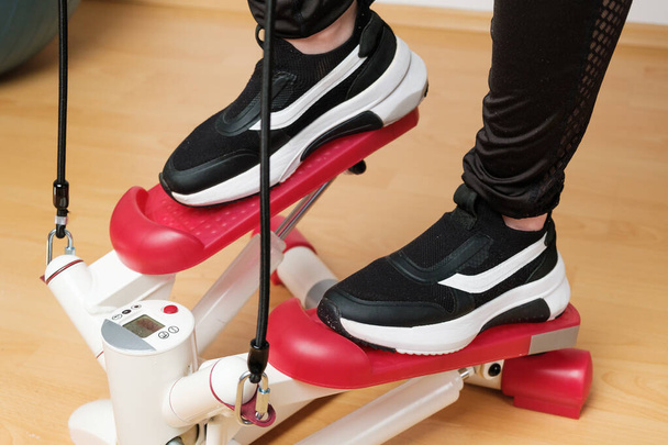 Acercamiento pies de las mujeres en zapatillas de deporte de entrenamiento en el paso de giro con pantalla digital y expansores de encías en casa durante el bloqueo.  - Foto, imagen