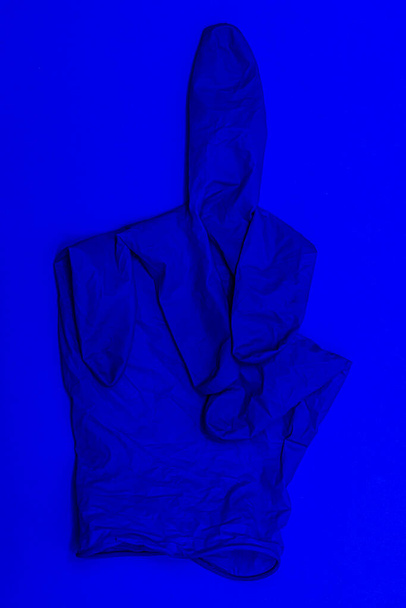 blue medical glove on the blue background fingers folded in an obscene fuck gesture - Foto, Imagen