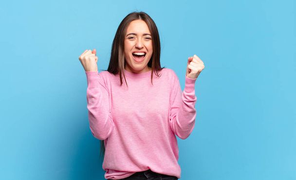 young pretty casual woman feeling happy, surprised and proud, shouting and celebrating success with a big smile - Фото, изображение