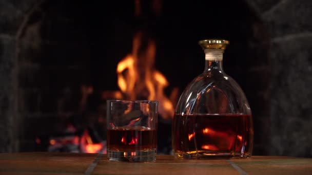 Fles en glas met whisky of cognac op de achtergrond van vuur in de open haard - Video