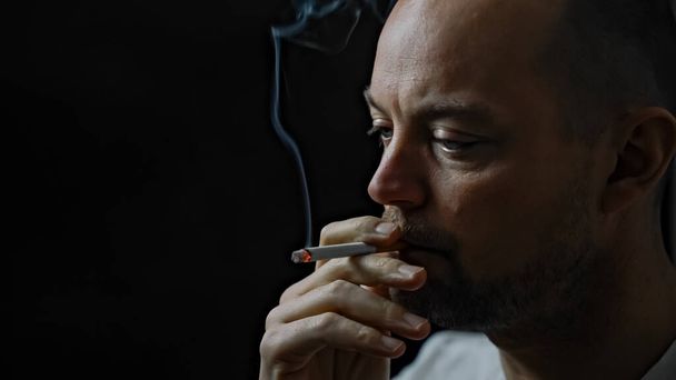 Sigara içen bir adama yaklaş. Siyah arkaplanda izole edilmiş, alan derinliği sığ. Yüksek kalite fotoğraf - Fotoğraf, Görsel