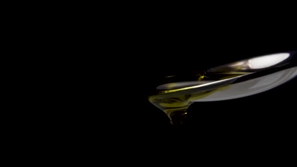 Goldenes Öl wird in Zeitlupe in einen metallenen Dessertlöffel gegossen. Makroschuss. Schwarzer Hintergrund - Filmmaterial, Video